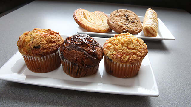 A plate of cookies in the background; a plate of 3 muffins in the foreground