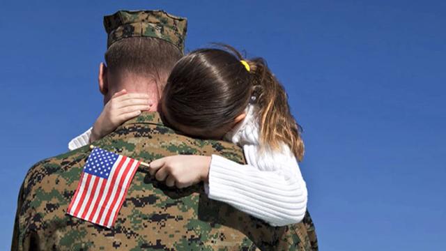 a young girl holding a flag hugs a soldier